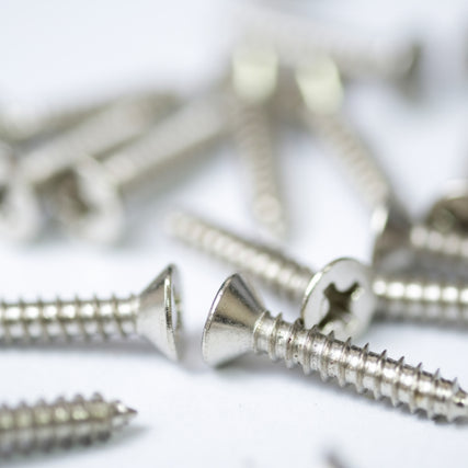 HardwareClose-up of several shiny silver screws with flat, slotted heads scattered on a white surface. The image conveys a sense of organization and utility.