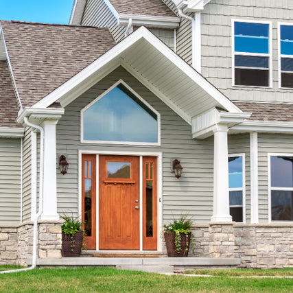 RoofingA modern suburban home with a gable roof, gray siding, and stone accents. A wooden front door is flanked by potted plants, conveying a welcoming tone.