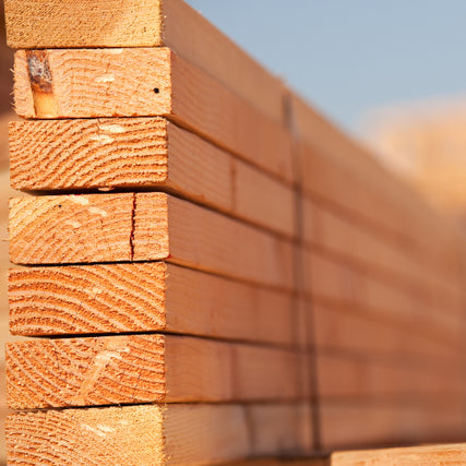 LumberStack of neatly arranged, light brown wooden planks lined vertically, showing natural wood grain and textures, under soft, warm daylight.
